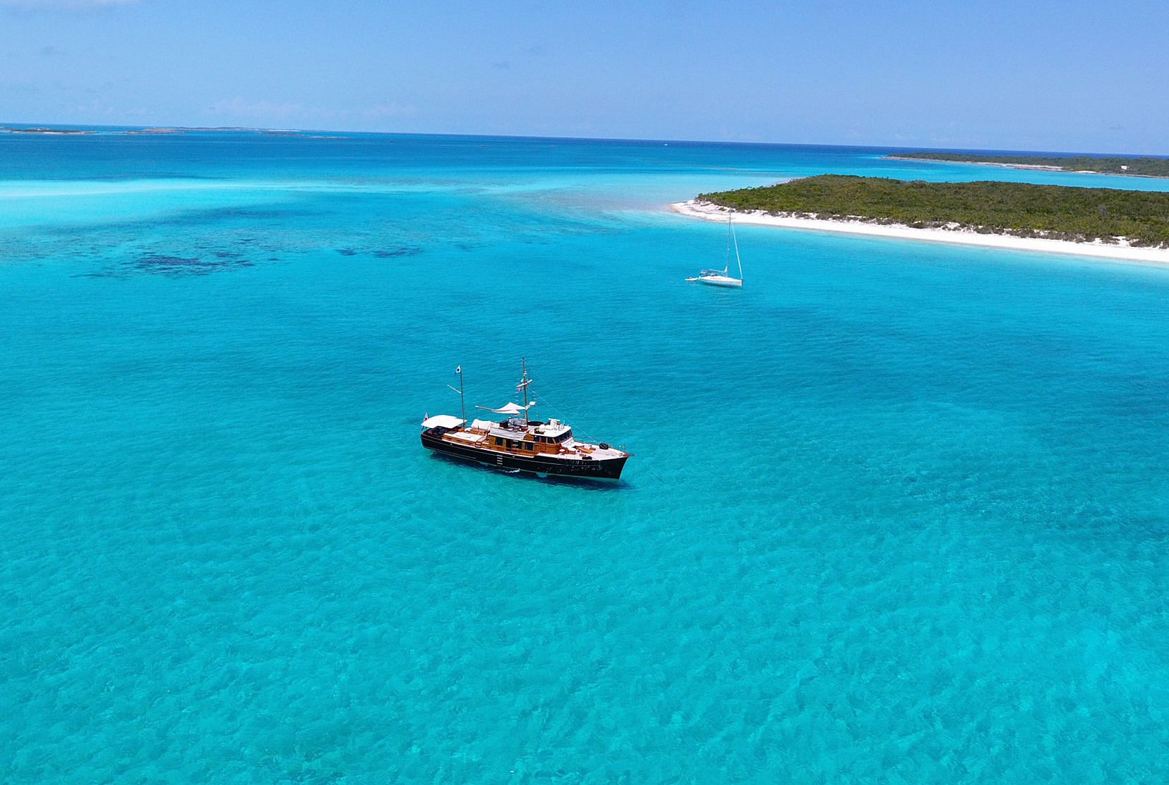 Small boat on bright turquoise sea near a sandy island coastline.