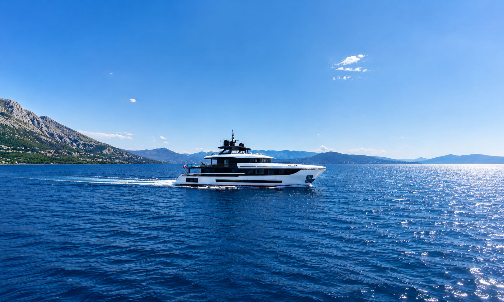 Luxury yacht cruising on a bright blue sea near a mountain coast